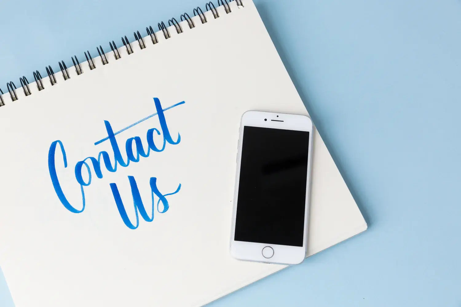 Mobile Phone laid on a white piece of paper with Contact Us written on it